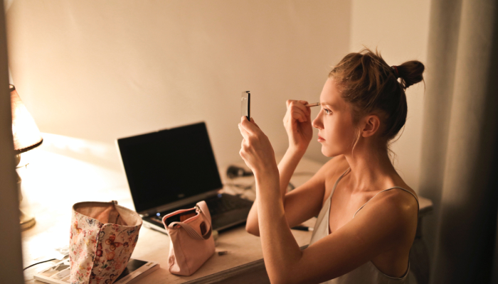 Mujer joven maquillándose delante del espejo.